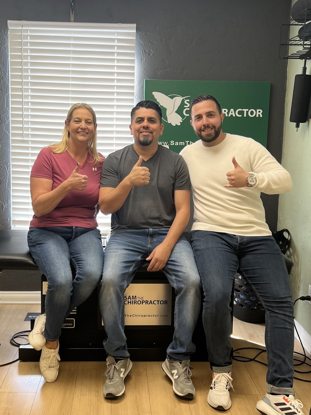 Three smiling patients giving thumbs up after their adjustments with Dr. Sam